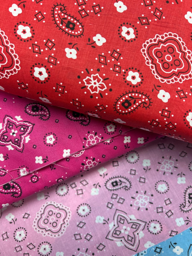 May include: Three pieces of fabric with a paisley bandana print. The top fabric is red with white and black paisley designs. The middle fabric is pink with white and black paisley designs. The bottom fabric is light pink with white and black paisley designs.