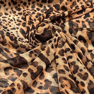 K&ouml;nnte beinhalten: Nahaufnahme eines Stoffes mit Leopardenmuster. Der Stoff ist ein transparentes Mesh-Material mit beigem Hintergrund und dunkelbraunen Flecken. Der Stoff ist gefaltet und erzeugt Schatten und Tiefe.