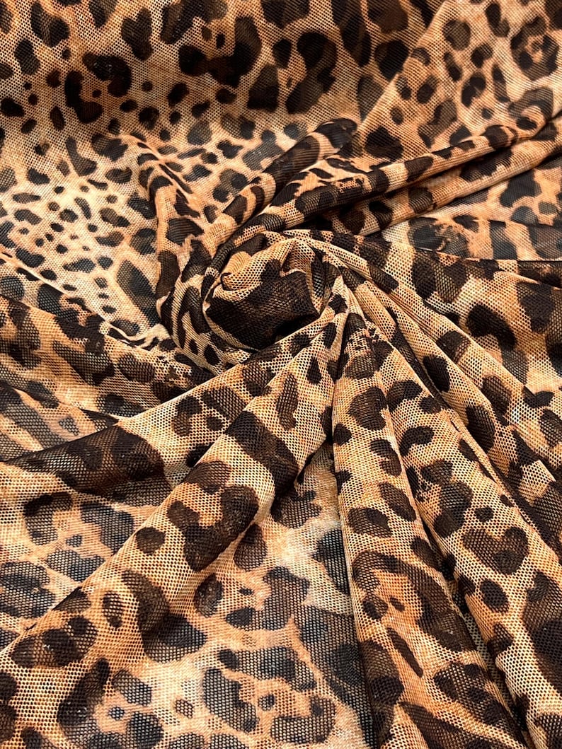 K&ouml;nnte beinhalten: Nahaufnahme eines Stoffes mit Leopardenmuster. Der Stoff ist ein transparentes Mesh-Material mit beigem Hintergrund und dunkelbraunen Flecken. Der Stoff ist gefaltet und erzeugt Schatten und Tiefe.