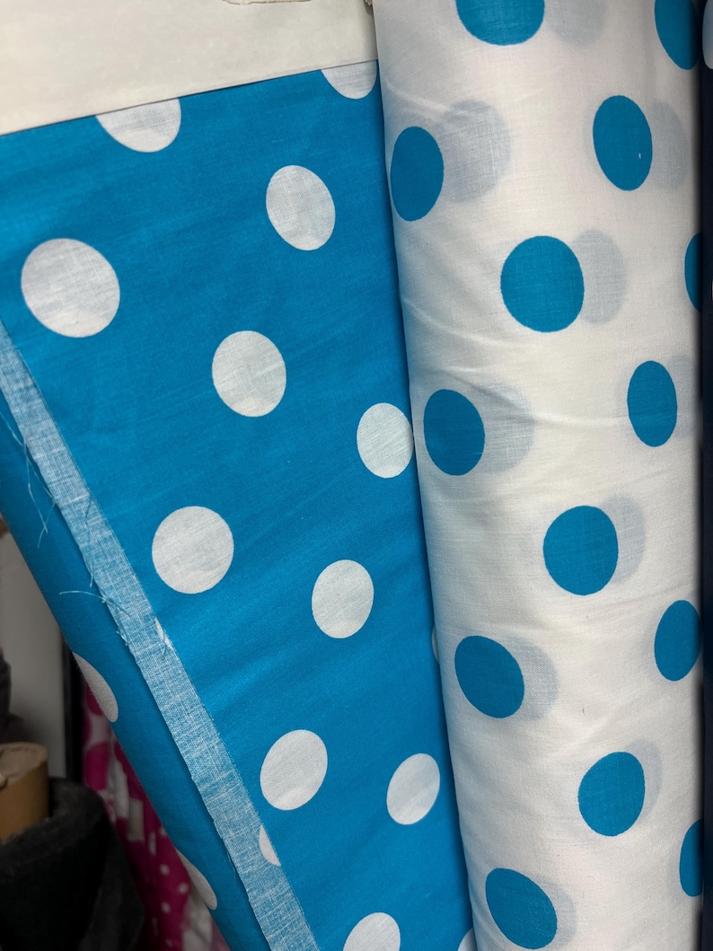 Puede incluir: Dos rollos de tela, uno en azul turquesa vibrante con grandes lunares blancos, y el otro en blanco con lunares turquesa. La tela est&aacute; enrollada, mostrando el dise&ntilde;o repetitivo. Ideal para proyectos de costura.