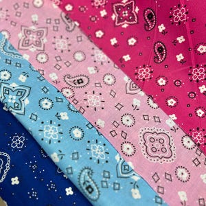 May include: Three fabric swatches with a paisley pattern. The top swatch is pink with white paisley designs. The middle swatch is light blue with white paisley designs. The bottom swatch is dark blue with white paisley designs.