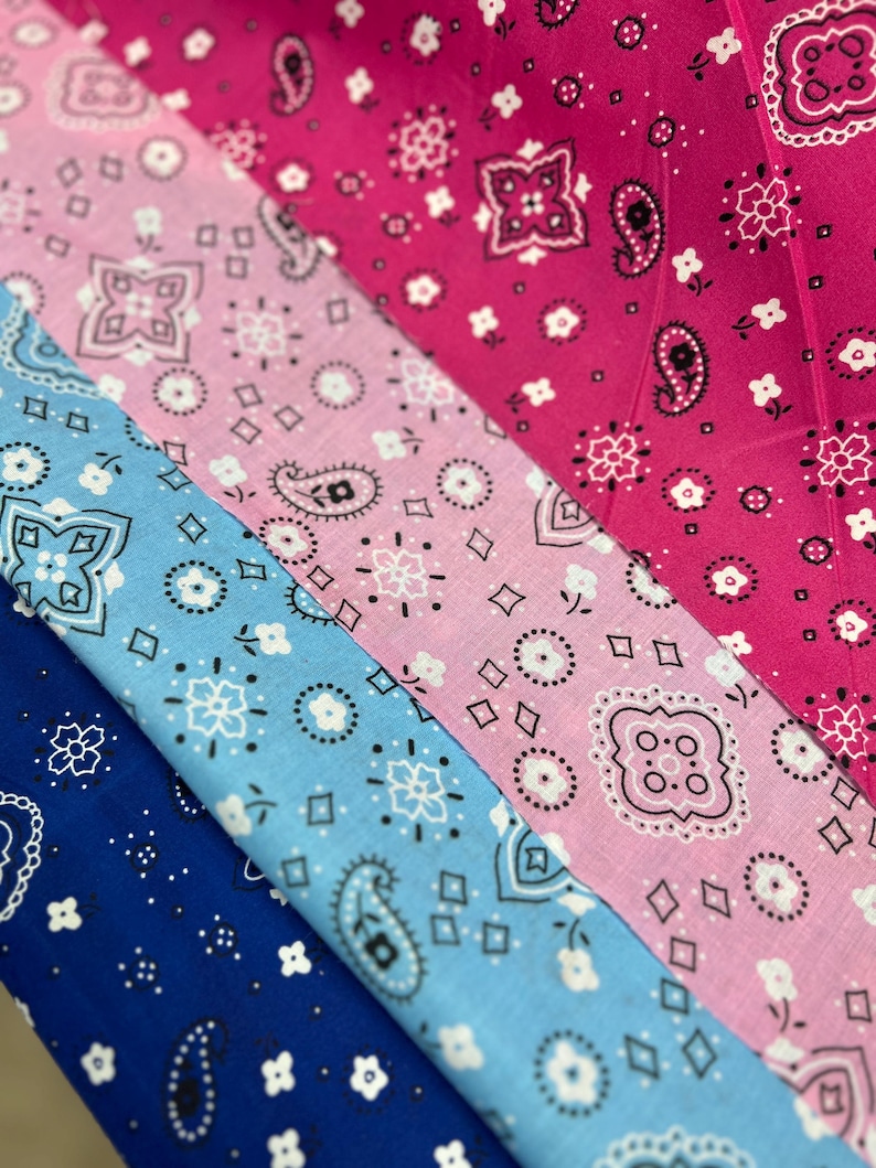 May include: Three fabric swatches with a paisley pattern. The top swatch is pink with white paisley designs. The middle swatch is light blue with white paisley designs. The bottom swatch is dark blue with white paisley designs.