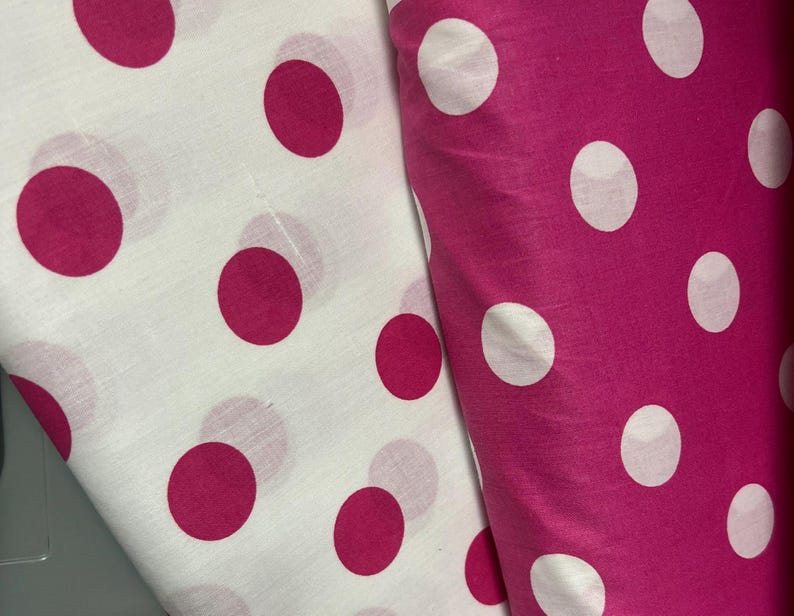 Puede incluir: Dos telas con un estampado de lunares. Una tela es blanca con grandes lunares magenta. La otra tela es magenta con grandes lunares blancos. Las telas est&aacute;n dobladas y superpuestas.