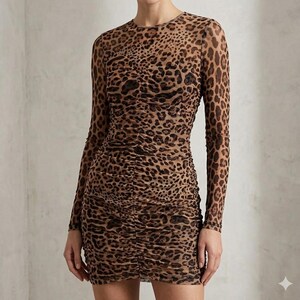 K&ouml;nnte beinhalten: Figurbetontes Kleid mit Leopardenmuster und langen &Auml;rmeln. Das Kleid hat einen runden Ausschnitt und geraffte Details auf der Vorderseite. Der Stoff ist ein transparentes Material mit einem braunen und schwarzen Animal-Print.
