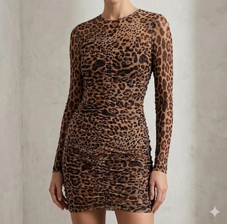 K&ouml;nnte beinhalten: Figurbetontes Kleid mit Leopardenmuster und langen &Auml;rmeln. Das Kleid hat einen runden Ausschnitt und geraffte Details auf der Vorderseite. Der Stoff ist ein transparentes Material mit einem braunen und schwarzen Animal-Print.