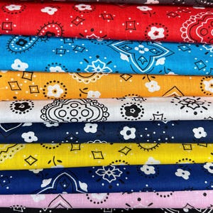 May include: A stack of ten colorful bandanas with paisley and diamond patterns. The bandanas are in various colors, including red, blue, yellow, white, black, and pink.