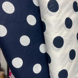 Puede incluir: Dos rollos de tela, uno azul marino con lunares blancos y otro blanco con lunares azul marino. La tela est&aacute; bien enrollada, mostrando claramente el patr&oacute;n. Los lunares son grandes y est&aacute;n espaciados uniformemente.