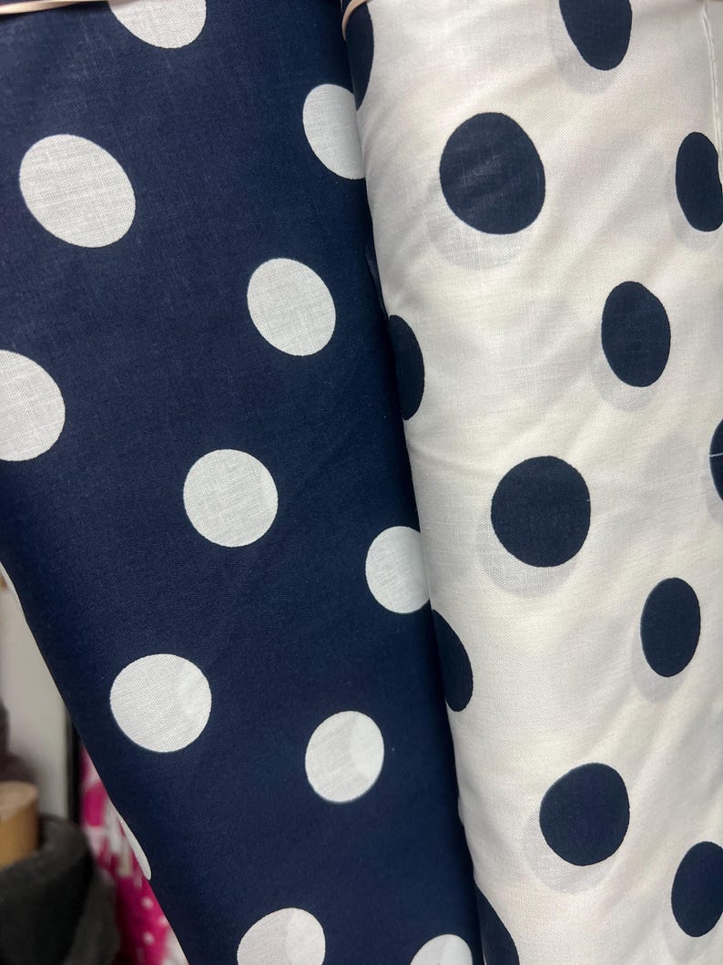Puede incluir: Dos rollos de tela, uno azul marino con lunares blancos y otro blanco con lunares azul marino. La tela est&aacute; bien enrollada, mostrando claramente el patr&oacute;n. Los lunares son grandes y est&aacute;n espaciados uniformemente.