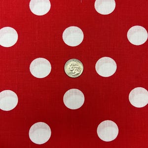 Puede incluir: Tela roja con lunares blancos grandes. Una moneda se coloca en la tela como referencia de tama&ntilde;o. La tela tiene un dise&ntilde;o cl&aacute;sico y juguet&oacute;n.