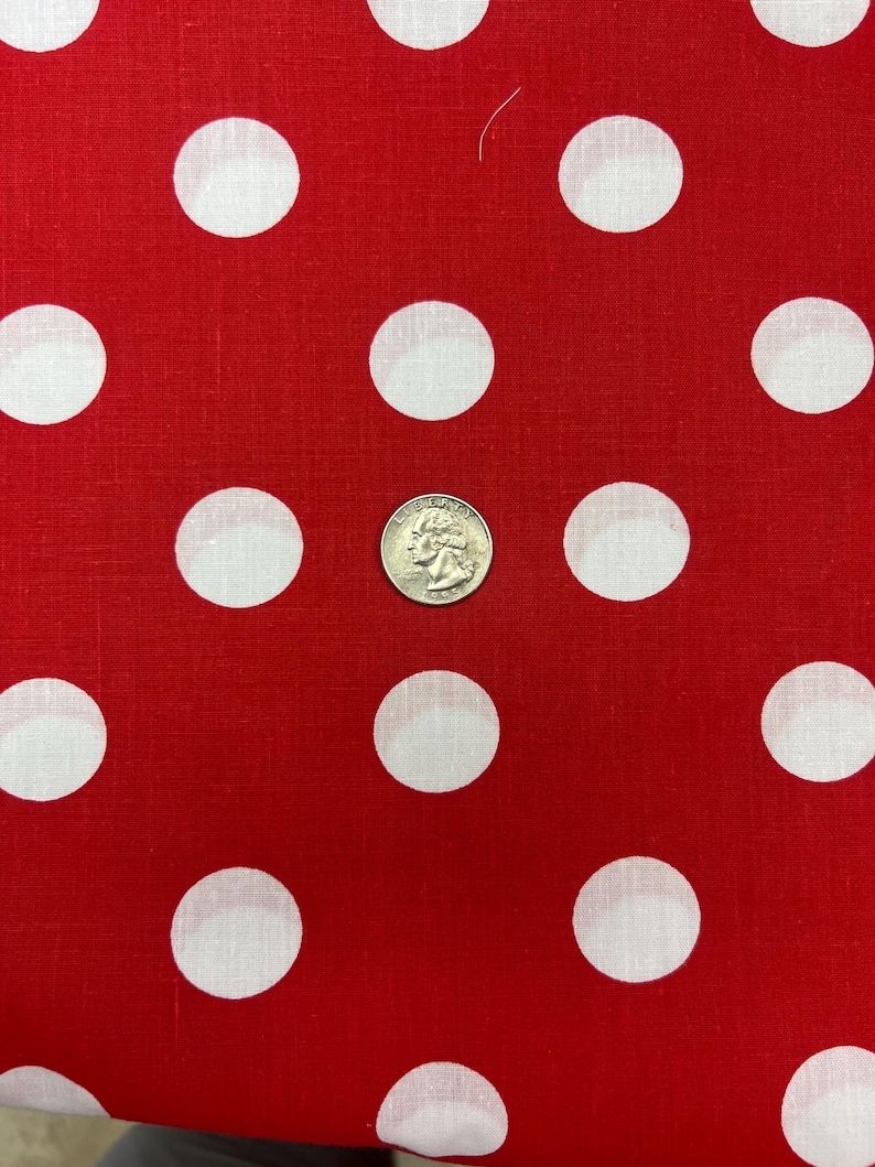 Puede incluir: Tela roja con lunares blancos grandes. Una moneda se coloca en la tela como referencia de tama&ntilde;o. La tela tiene un dise&ntilde;o cl&aacute;sico y juguet&oacute;n.