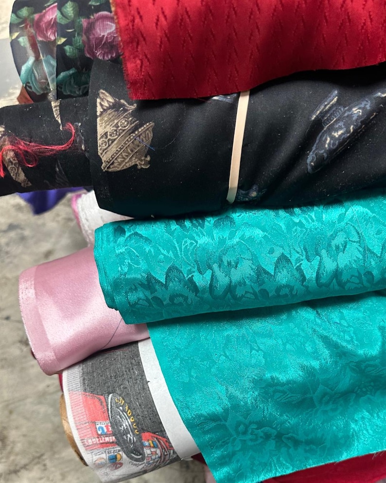 Puede incluir: Un rollo de tela rojo, un rollo negro con una franja blanca, un rollo turquesa con estampado floral, un rollo rosa y un rollo con estampado colorido.