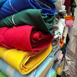 Puede incluir: Un mont&oacute;n de rollos de tela de colores en varios tonos de azul, verde, rojo, amarillo y azul claro. Los rollos de tela est&aacute;n apilados ordenadamente y dispuestos en un patr&oacute;n vertical.