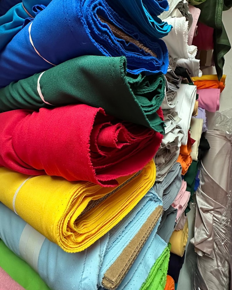 Puede incluir: Un mont&oacute;n de rollos de tela de colores en varios tonos de azul, verde, rojo, amarillo y azul claro. Los rollos de tela est&aacute;n apilados ordenadamente y dispuestos en un patr&oacute;n vertical.
