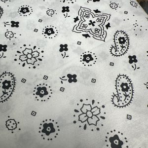 May include: A white fabric with a black paisley pattern. The pattern includes flowers, paisley shapes, and small dots.