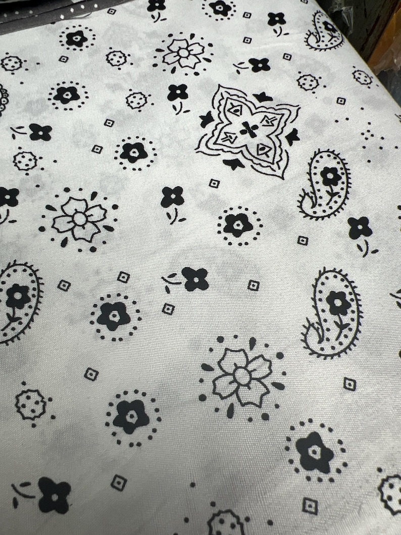 May include: A white fabric with a black paisley pattern. The pattern includes flowers, paisley shapes, and small dots.