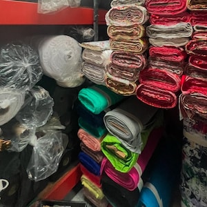 Puede incluir: Una variedad de rollos de tela en diferentes colores y patrones, incluyendo blanco, rojo, verde, azul y rosa. Los rollos est&aacute;n apilados en estantes en una tienda minorista.