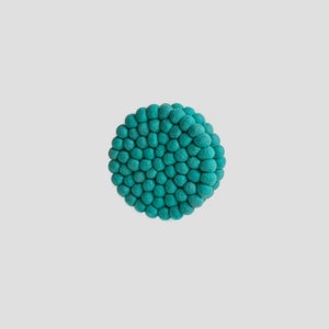 May include: Teal blue felt coaster with a round shape and a textured surface made of small, round balls.