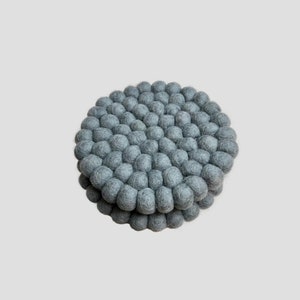 May include: Two grey felt coasters with a round shape and a textured surface. The coasters are made of small, round felt balls.