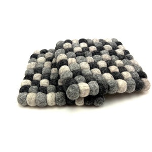 May include: Two gray and black felt coasters made of small, round balls. The coasters are stacked on top of each other.