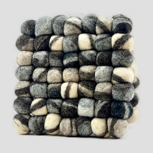 May include: A square-shaped coaster made of felted wool balls in shades of gray, black, and white. The balls are arranged in a grid pattern, creating a textured surface.