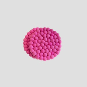 Può includere: Un sottobicchiere in feltro rosa fatto di piccoli pompon rotondi. Il sottobicchiere è circolare e ha un diametro di circa 25 cm.