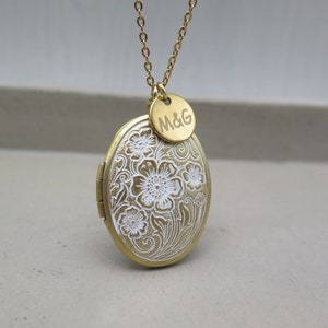 Könnte beinhalten: Goldene Halskette mit Anhänger, verziert mit einem weißen Blumenmuster und einem kleinen runden Anhänger mit der Gravur "M&G".