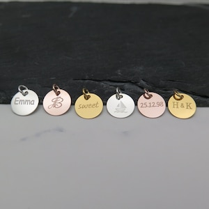 Könnte beinhalten: Sieben runde Anhänger aus Silber, Gold und Roségold mit verschiedenen Gravuren. Die Anhänger sind mit den Worten "Emma", "B", "sweet", "25.12.98", "H & K" und einem Segelboot graviert.