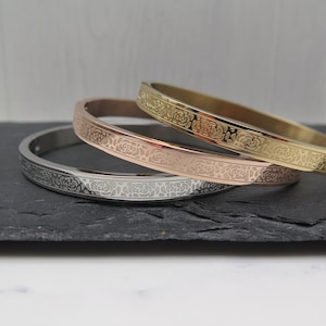 Könnte beinhalten: Drei Edelstahl-Armbänder mit Rosenmuster. Die Armbänder sind übereinander gestapelt, wobei das goldene Armband oben, das roségoldene Armband in der Mitte und das silberne Armband unten liegt.