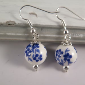 Peut inclure: Une paire de boucles d'oreilles pendantes en argent avec des perles en céramique blanche ornées d'un motif floral bleu.