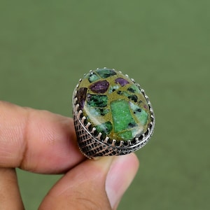 Könnte beinhalten: Ein silberner Ring mit einem grünen, goldenen und violetten Edelstein. Der Edelstein ist in einer silbernen Fassung gefasst und hat ein strukturiertes Design.