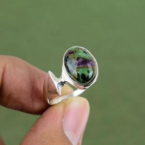 May include: A silver ring with a green and purple gemstone. The ring has a unique, abstract design.