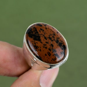 Pode incluir: Um anel de prata com uma grande pedra ovalada de cor marrom e preta. A pedra tem um padrão manchado de marrom e preto.