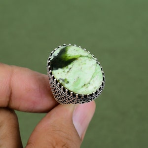 May include: A silver ring with a green oval gemstone set in a decorative filigree design.