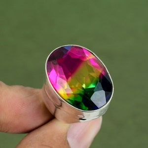 Op de afbeelding: Een zilveren ring met een grote ovale edelsteen. De edelsteen is een mix van roze, gele, groene en blauwe kleuren.