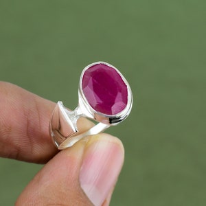 May include: A silver ring with a large, oval-shaped ruby gemstone. The ruby is a deep red color and has a faceted cut.