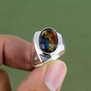 May include: A silver ring with a large oval-shaped gemstone. The gemstone is iridescent and has shades of blue, green, and brown.
