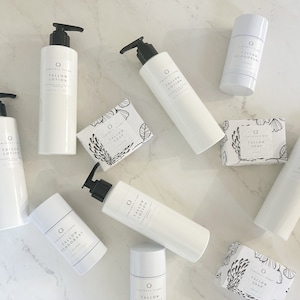 May include: A collection of white bottles and containers with black labels and text that reads "Tallow Lotion", "Tallow Deodorant", and "Tallow Soap". The products are arranged on a white marble surface.