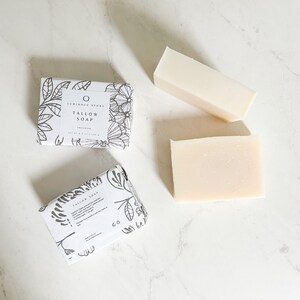 Puede incluir: Dos barras de jab&oacute;n de sebo blanco con un dise&ntilde;o floral en el empaque. El empaque dice "Luminous Stone Tallow Soap, Organic".
