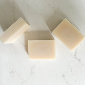 Puede incluir: Tres barras rectangulares de jab&oacute;n blanco sobre una superficie de m&aacute;rmol blanco.