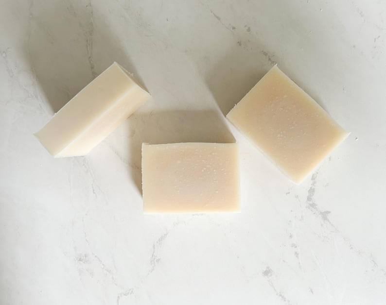 Puede incluir: Tres barras rectangulares de jab&oacute;n blanco sobre una superficie de m&aacute;rmol blanco.
