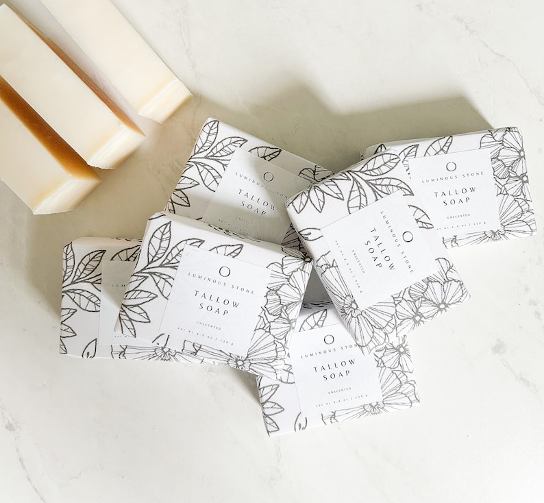 Puede incluir: Cinco barras de jab&oacute;n blanco con dise&ntilde;os florales negros y el texto "LUMINOUS STONE TALLOW SOAP" en cada barra.