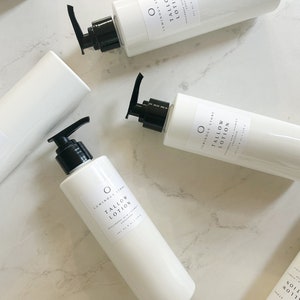 May include: Four white bottles of  Luminous Store Tallow Lotion, a moisturizing skin care product. The bottles are on a white marble surface.