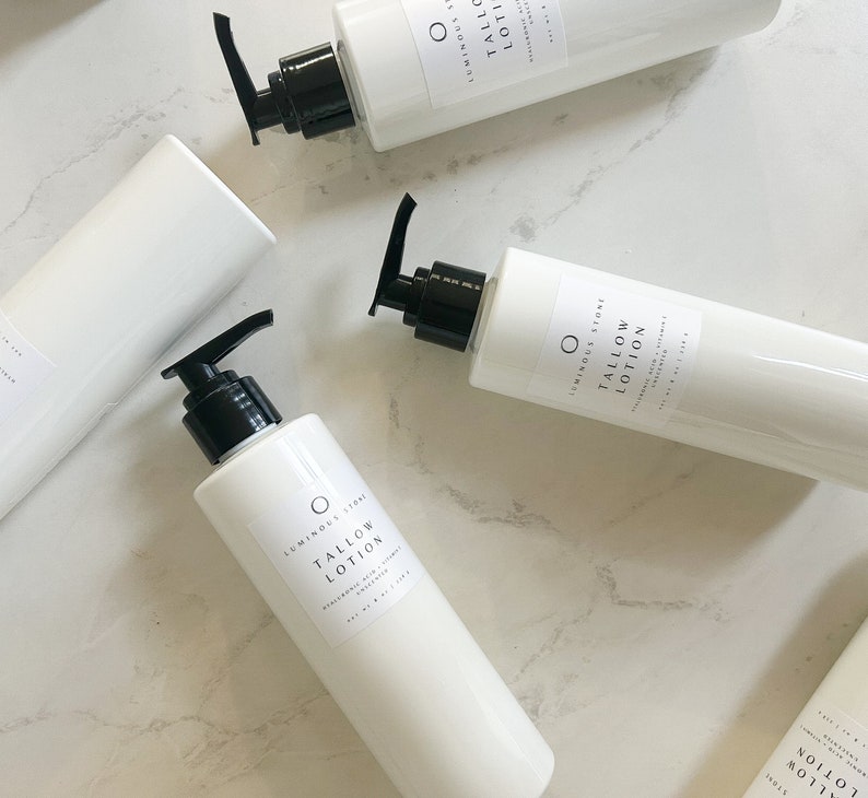 May include: Four white bottles of  Luminous Store Tallow Lotion, a moisturizing skin care product. The bottles are on a white marble surface.