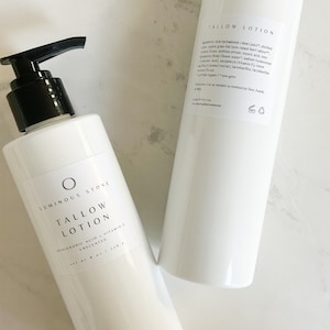 May include: Two white bottles of unscented tallow lotion with black pump tops. The bottle on the right has the ingredients listed on the back. The bottle on the left has the brand name "Luminous Stone" and the text "Tallow Lotion" printed on the front.