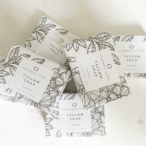 Puede incluir: Cinco barras de jab&oacute;n blanco con dise&ntilde;os florales negros y el texto "Luminous Stone Tallow Soap Unscented" en cada barra.
