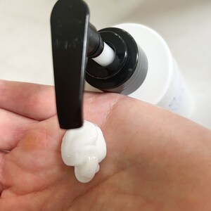 May include: A white pump bottle with a black pump dispenser. A dollop of white lotion is being dispensed onto a hand.