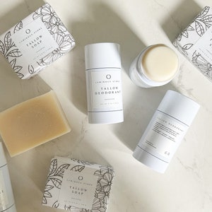 Puede incluir: Una vista plana de varios productos de belleza naturales de Luminous Stone. Los productos incluyen una barra de jab&oacute;n de sebo, un desodorante en barra y una caja de jab&oacute;n de sebo. Los productos son todos blancos y tienen texto negro. El fondo es una superficie de m&aacute;rmol blanco.