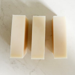 Puede incluir: Tres barras rectangulares de jab&oacute;n blanco, dispuestas una al lado de la otra sobre una superficie blanca.