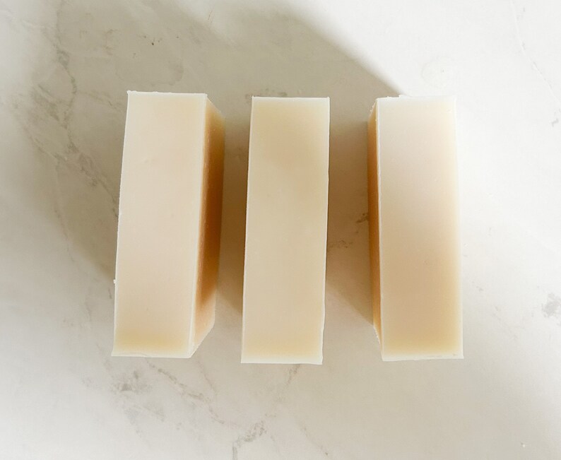 Puede incluir: Tres barras rectangulares de jab&oacute;n blanco, dispuestas una al lado de la otra sobre una superficie blanca.