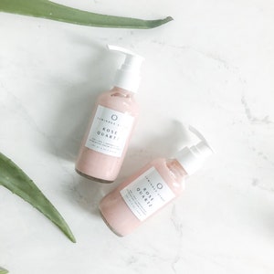 May include: Two pink glass bottles with white pumps and labels that read "Luminous Stone Rose Quartz Face and Body Cream Moisturizer".